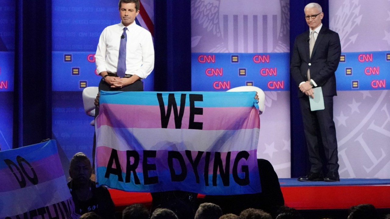 Democratic presidential candidate South Bend, Indiana Mayor Pete Buttigieg (L) and CNN moderator Anderson Cooper react as protestors display banners at the Human Rights Campaign Foundation and CNN’s presidential town hall focused on LGBTQ issues on Octobe