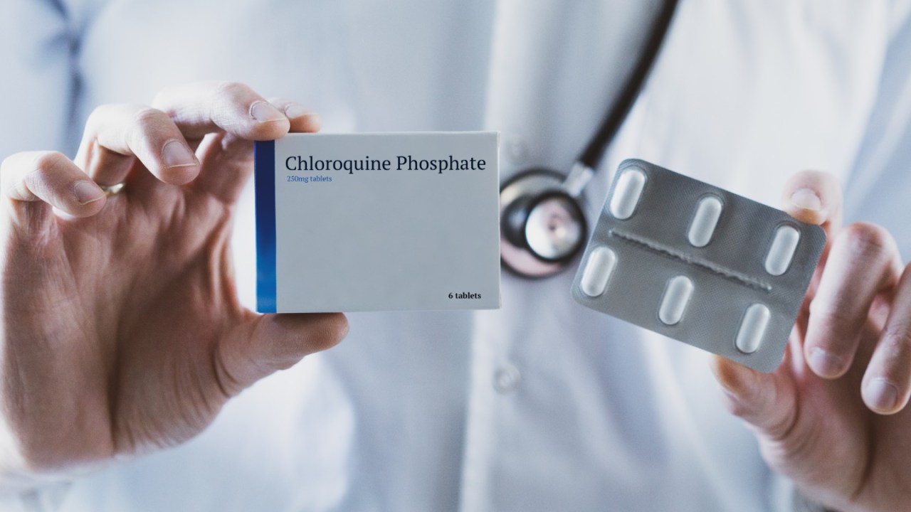 a doctor holds up a box of chloroquine phosphate with four tablets