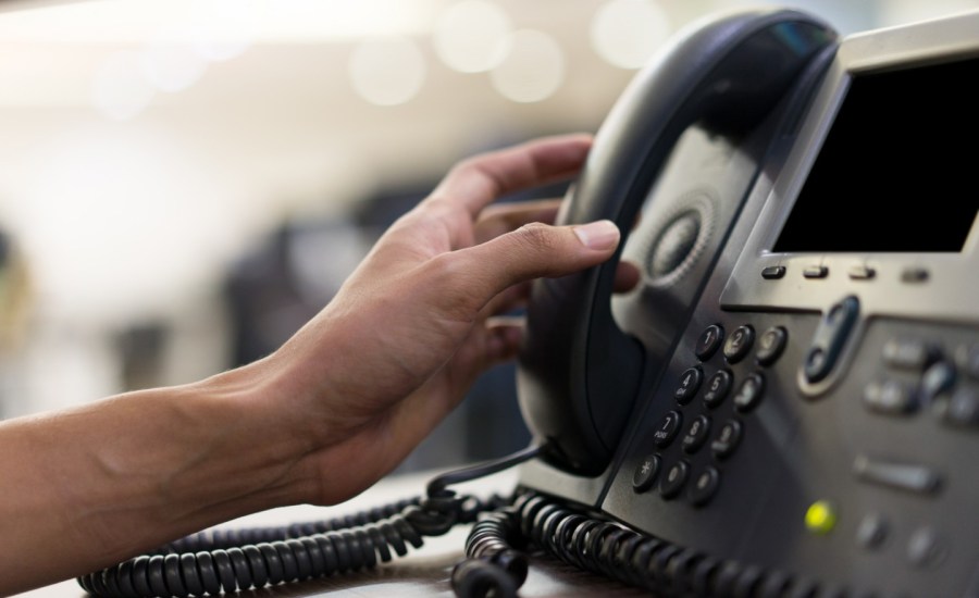 a person's hand reaches for a phone where a green dot marks an occupied line