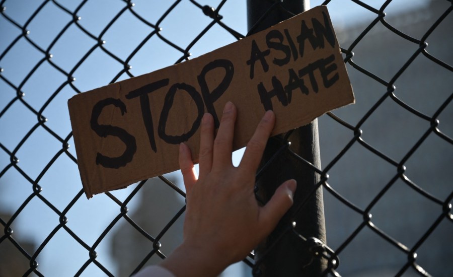 Members and supporters of the Asian-American community attend a "rally against hate" at Columbus Park in New York City on March 21, 2021. A person's hand holds a cardboard sign that reads "Stop AAPI Hate" against a fence.