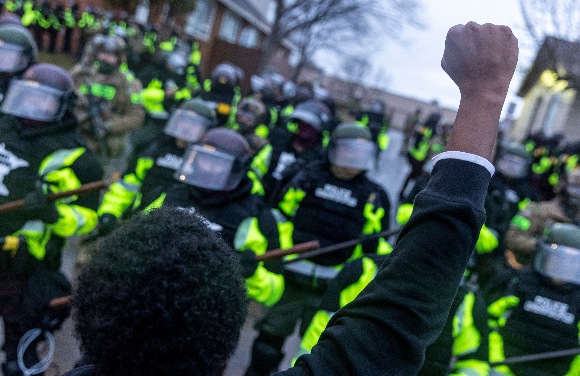 A man raises his fist as he faces the Minnesota State Troopers standing guard outside the Brooklyn Center Police Station