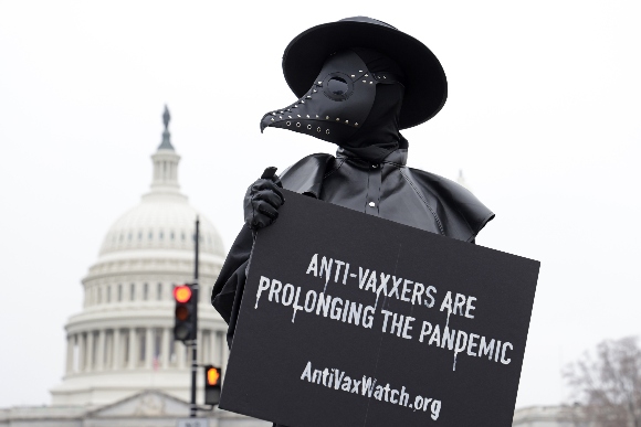 A man holds a sign and dresses as a plague doctor to encourage people to be vaccinated