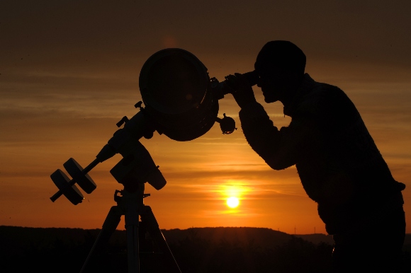 A hobby astronomer points his telescope at the yellow disk of the rising sun