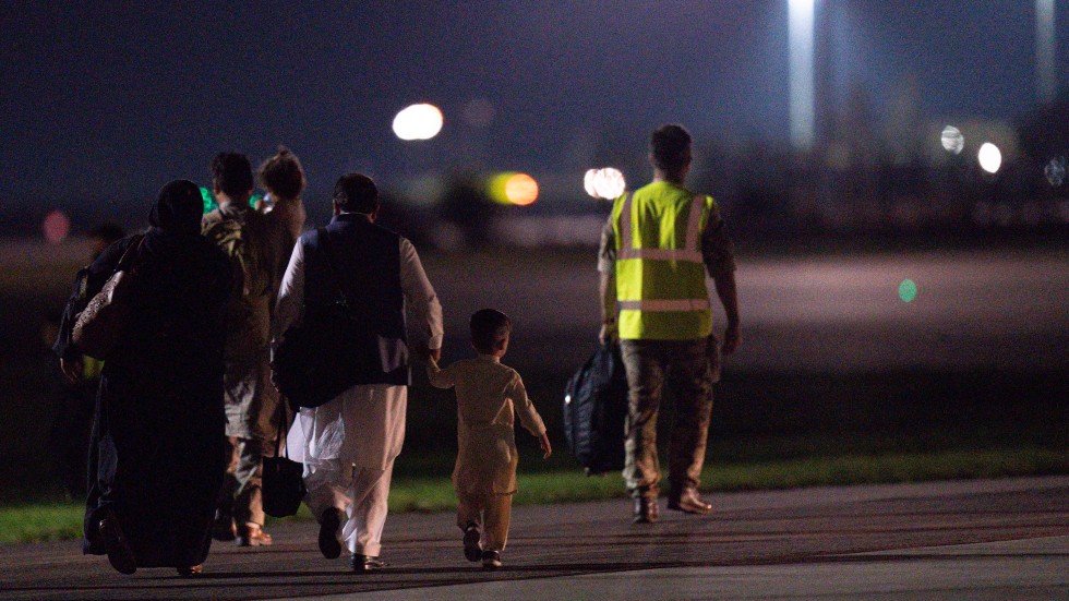 Passengers evacuated from Afghanistan are escorted across the tarmac after disembarking a British military transport aircraft at RAF Brize Norton station in southern England