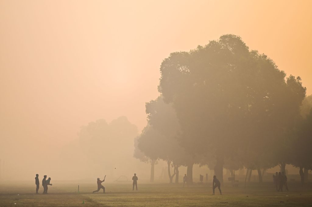 People play cricket in India in a cloud of smog