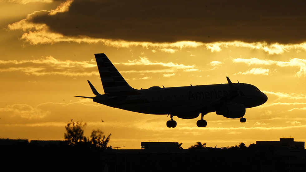 An American Airlines jet comes in for a landing at Miami International Airport against a orange sky