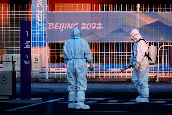 A worker wearing a protective suit sprays disinfectant at a screening checkpoint for arriving athletes at the 2022 Winter Olympics