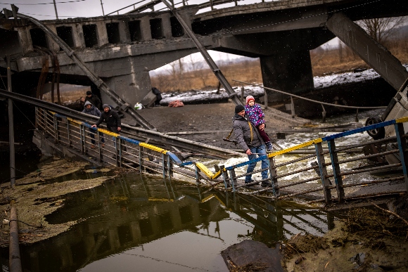 Local militiaman Valery, 37, carries a child as he helps a fleeing family across a bridge destroyed by artillery, on the outskirts of Kyiv