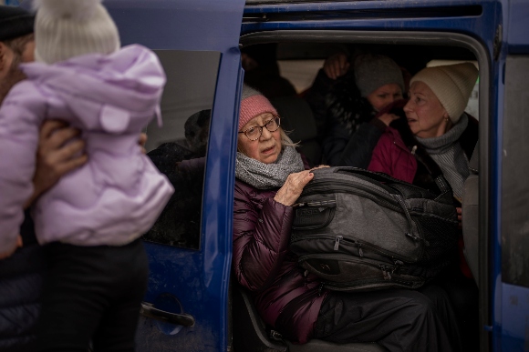 Ukrainian women sit inside a van as artillery echoes nearby, as people flee Irpin