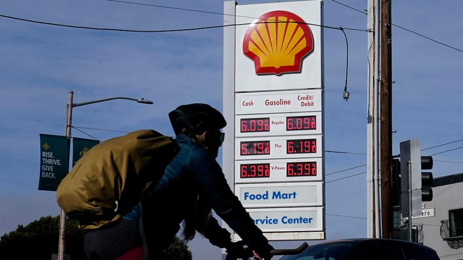 A bicyclist rides past a price board at a gas station