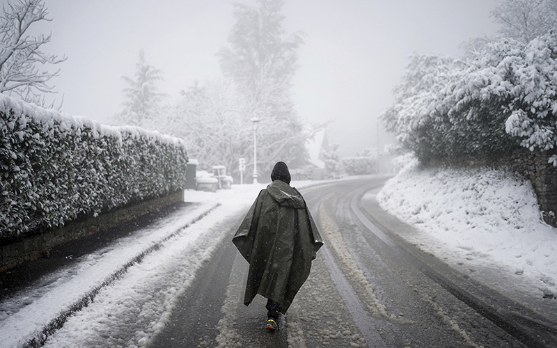 A woman, center, walks in winter gear down a snowy road