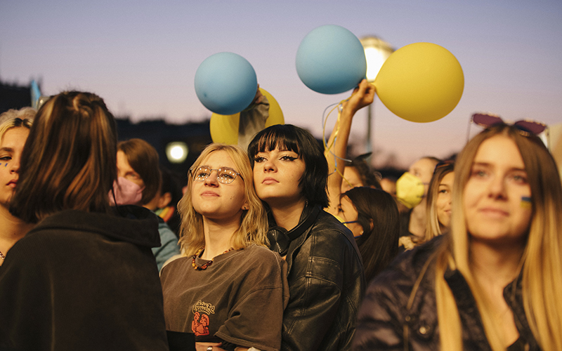 Two women hold each other as others hold yellow and blue balloons during a protest