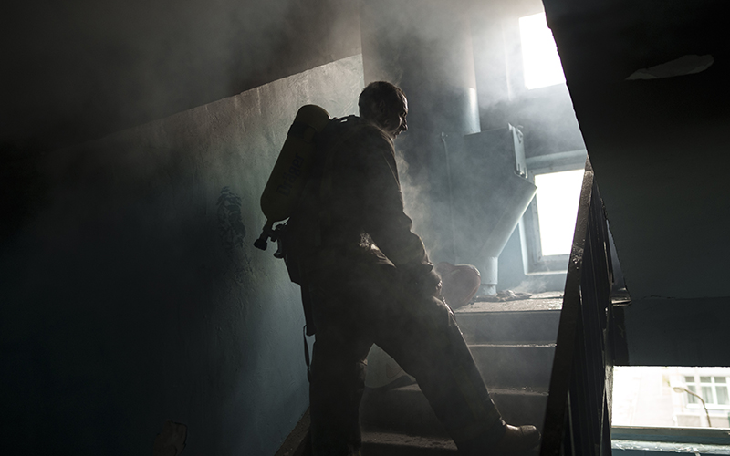 A firefighter pauses to cool down while extinguishing a fire as smoke lingers in the air