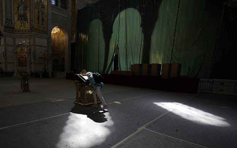 A woman kisses an icon in the St. Sava Serbian Orthodox temple as light filters through windows from above