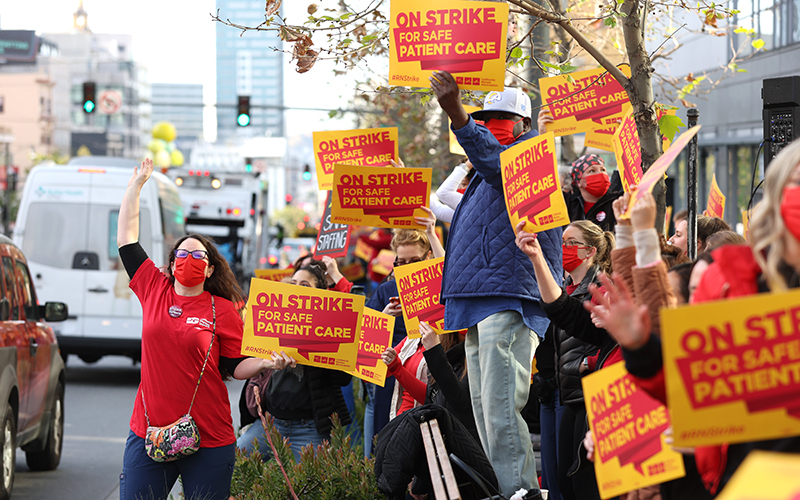 Sutter Health nurses and health care workers hold yellow and red signs reading "On strike for safe patient care"