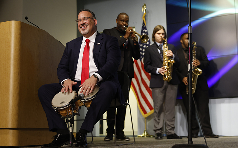 Education Secretary Miguel Cardona, front, plays Latin percussion while performing with acclaimed jazz artist Sean Jones