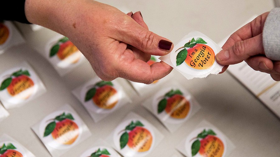 A poll worker hands a Georgia voting sticker to a voter