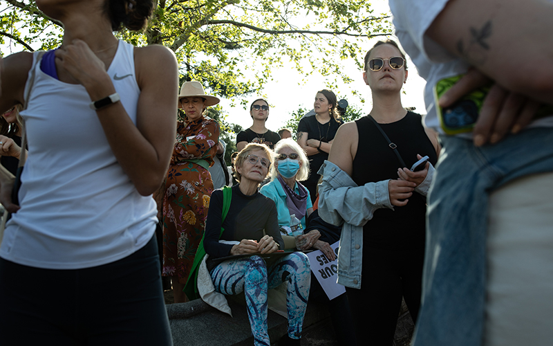 Protesters gather in front of the Supreme Court with some sitting and some standing