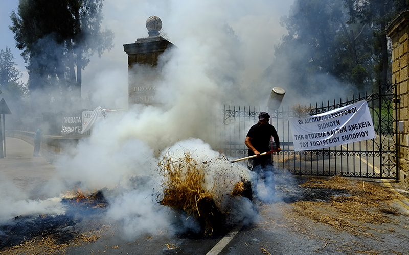 A farmer tries to control burning bales of hay outside the entrance gates, marked with a sign, of Cyprus's presidential palace