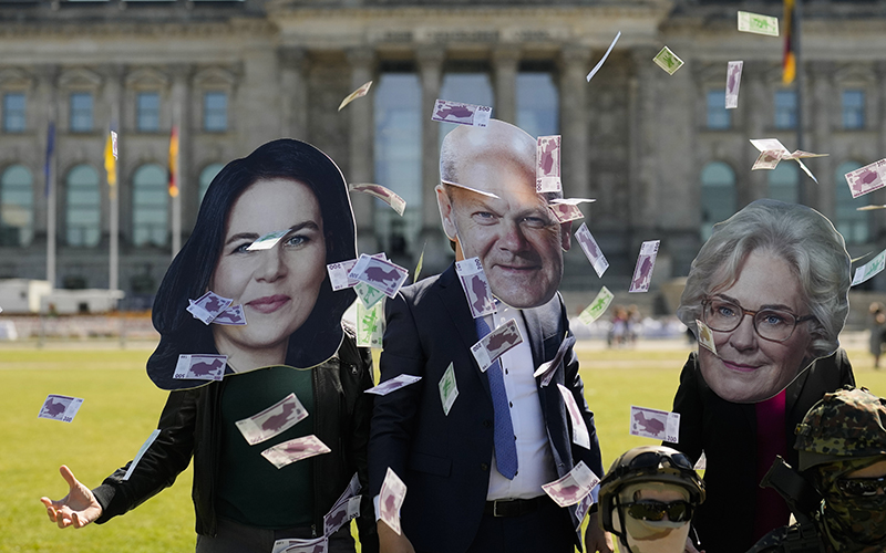 Demonstrators wear masks of Annalena Baerbock, from left, Olaf Scholz and Christine Lambrecht as they throw fake money with the Reichstag building in the background