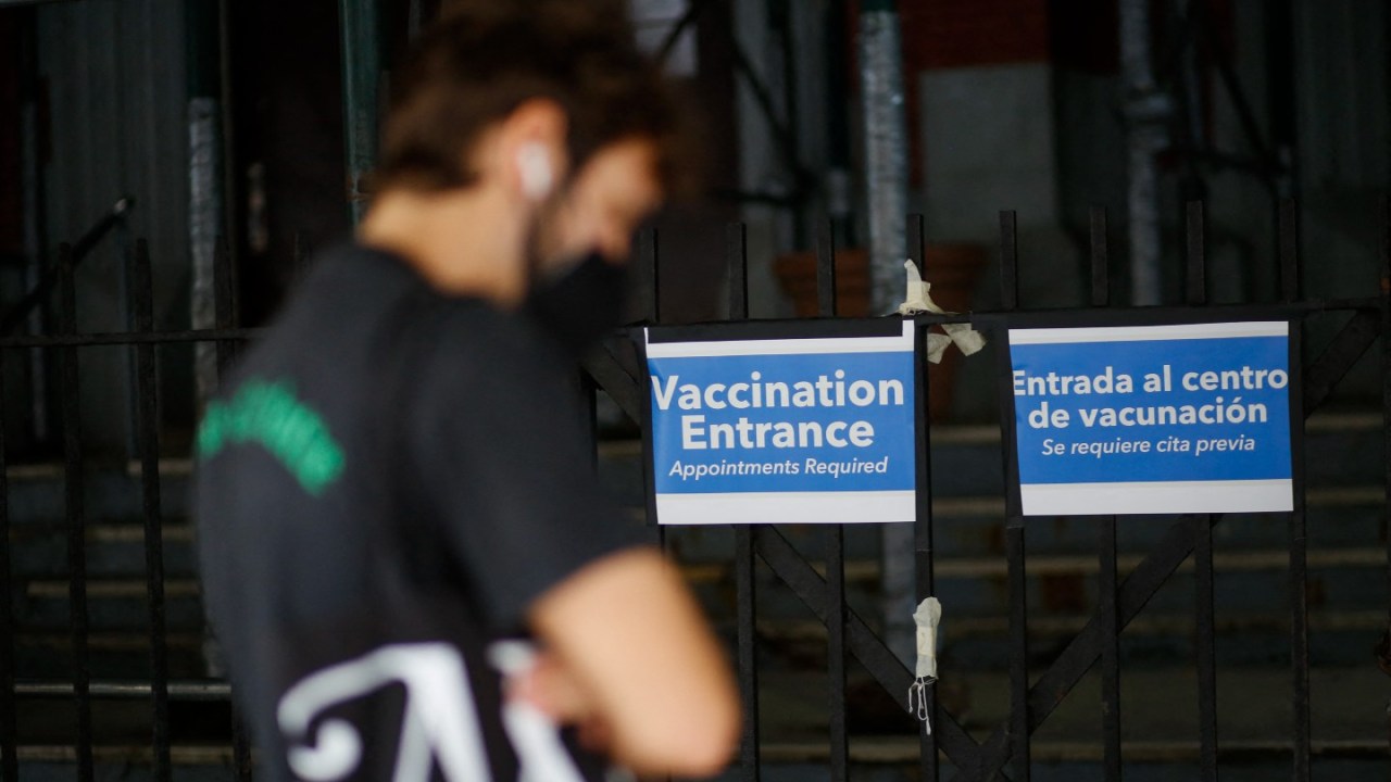 blurry image of man waiting outside, sign saying vaccination entrance in background