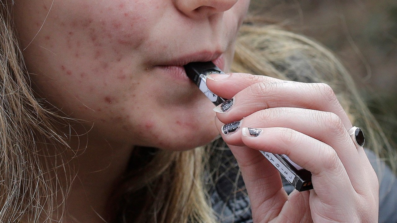 A teenager smokes a vaping device.