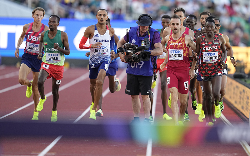 Men race around a camera person on the track