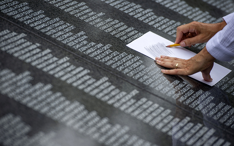 A woman etches a name from the Wall of Remembrance