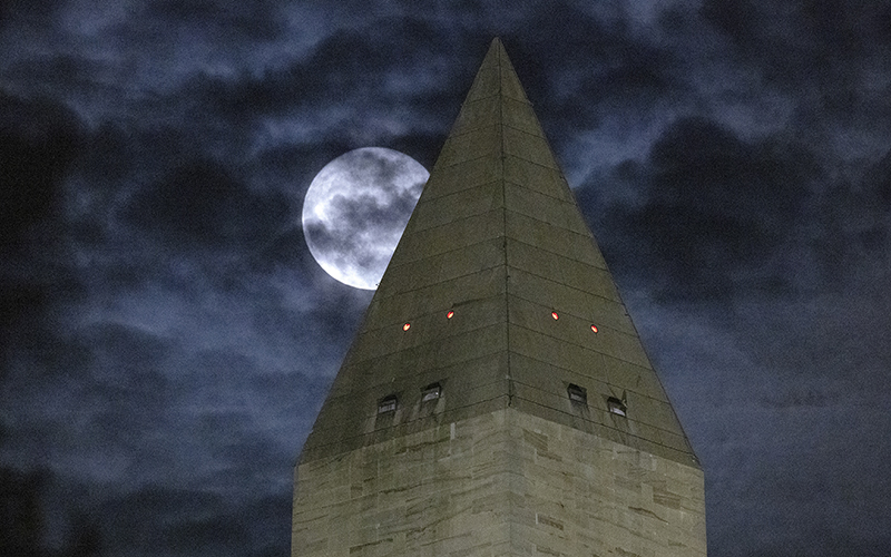 The moon is obscured by clouds as it passes behind the Washington Monument