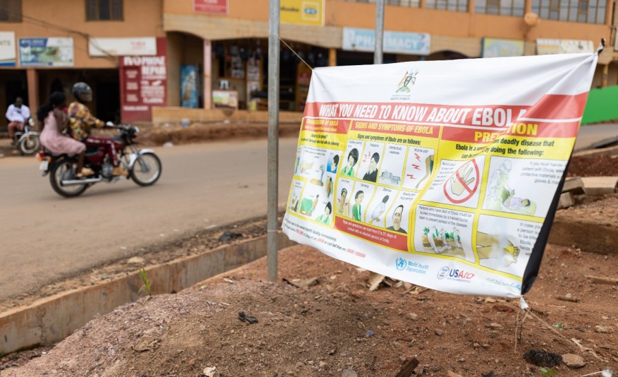 street with people on motorcycle next to a sign saying "what you need to know about ebola"