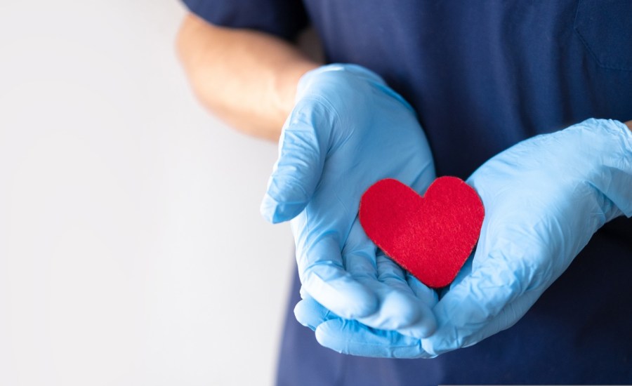 medical professional wearing gloves holding a paper cutout of a red heart shape