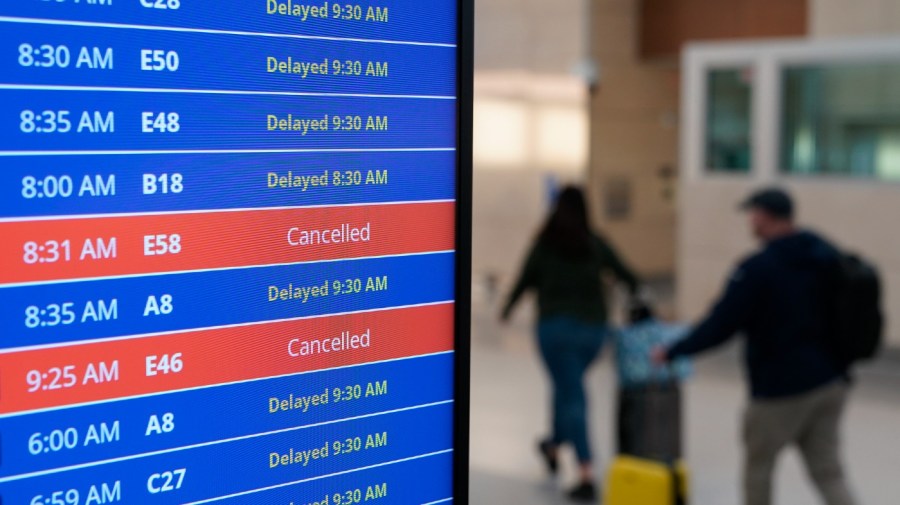 Travelers walk as a video board shows flight delays and cancellations at Ronald Reagan Washington National Airport in Arlington, Va., Wednesday, Jan. 11, 2023. (AP Photo/Patrick Semansky)