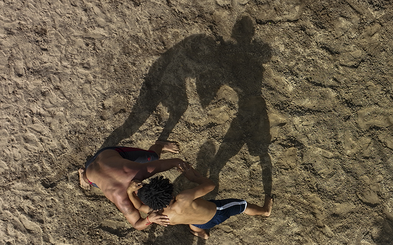 Athletes competing in a Brazilian Indigenous wrestling event cast shadows on the dirt