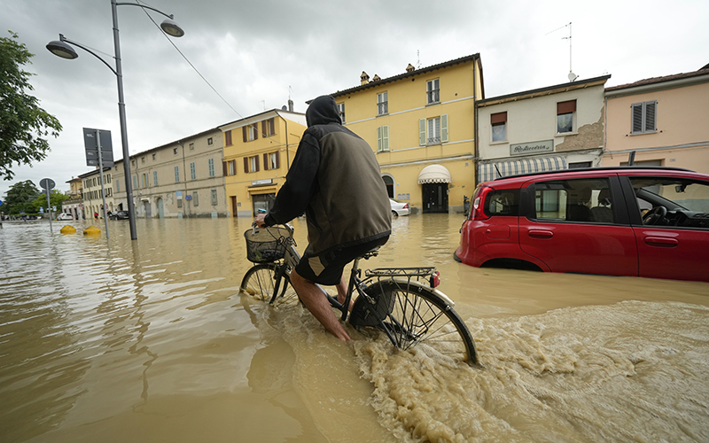 A cyclist rides through a flooded street in the village of Castel Bolognese. A red car, right, is seen stalled in the floodwaters