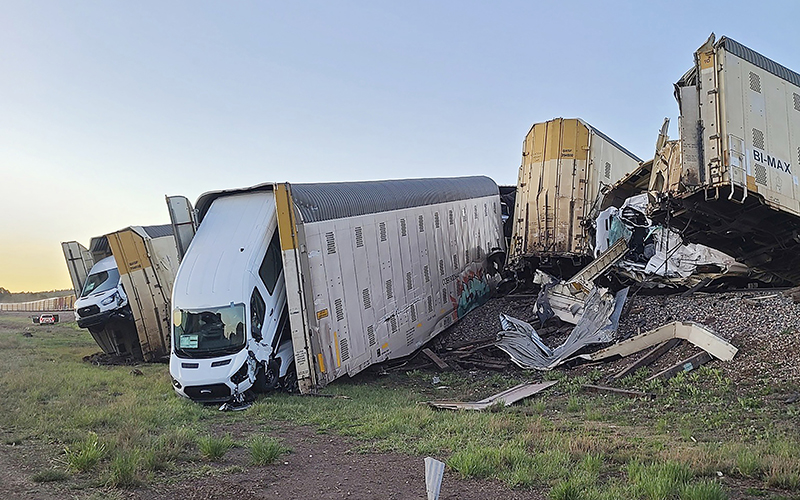 Damaged vehicles and other cargo spill out of derailed train cars