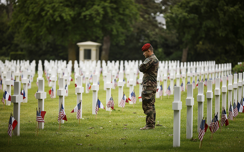 A soldier stands amid white cross headstones at the American Cemetery during a ceremony to commemorate D-Day