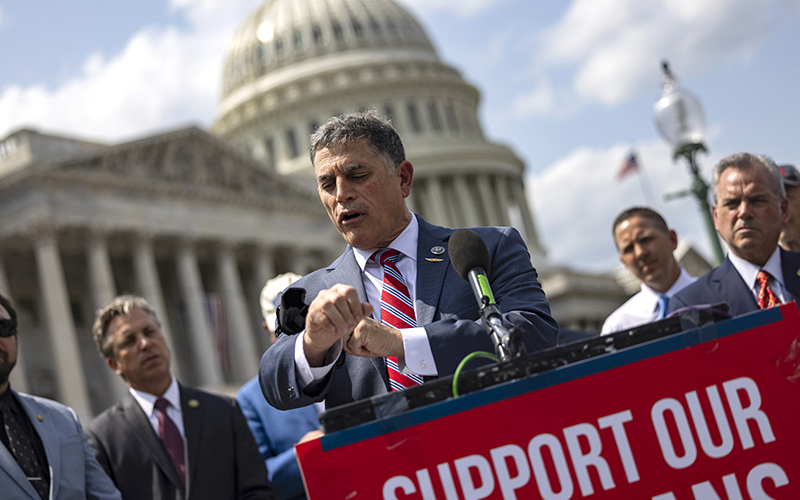 Rep. Andrew Clyde (R-Ga.) speaks during a press conference, checking his watch, while several others look on. The Capitol is seen in the background.