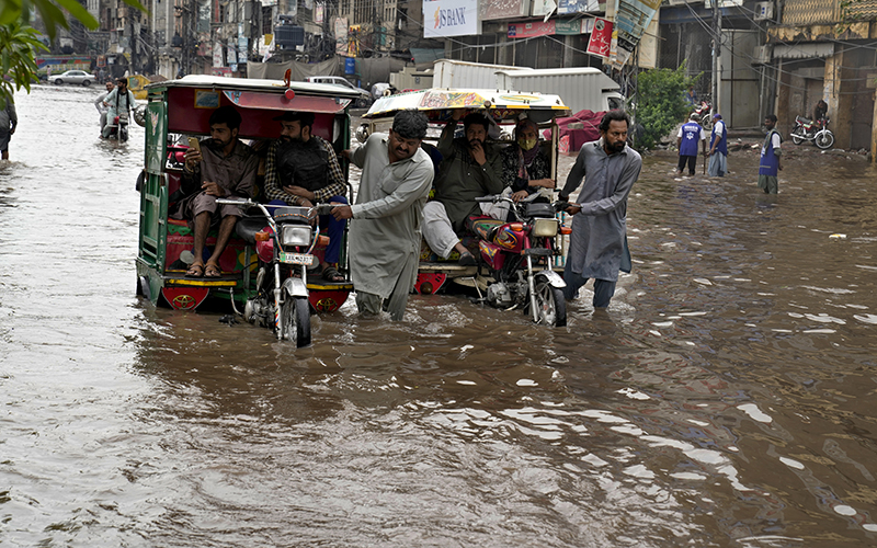 Drivers push their motorcycle rickshaws through a flooded road