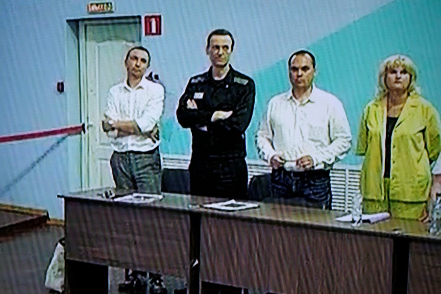 Russian opposition leader Alexei Navalny, 2nd left, is seen on a TV screen standing among his lawyers, as he appears in a video link provided by the Russian Federal Penitentiary Service, during a hearing in the colony, in Melekhovo, Vladimir region, about 260 kilometers (163 miles) northeast of Moscow, Russia, on Friday, Aug. 4, 2023. Navalny on Friday was convicted on extremism charges and sentenced to 19 years in prisons, in the harshest ruling against the imprisoned Kremlin critic to date. (AP Photo/Alexander Zemlianichenko)