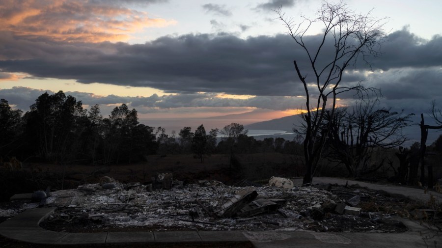 A home burned to ashes is seen in foreground as the sunset colors the sky in Kula, Hawaii, Tuesday, Aug. 15, 2023, following wildfires that devastated parts of the Hawaiian island of Maui.