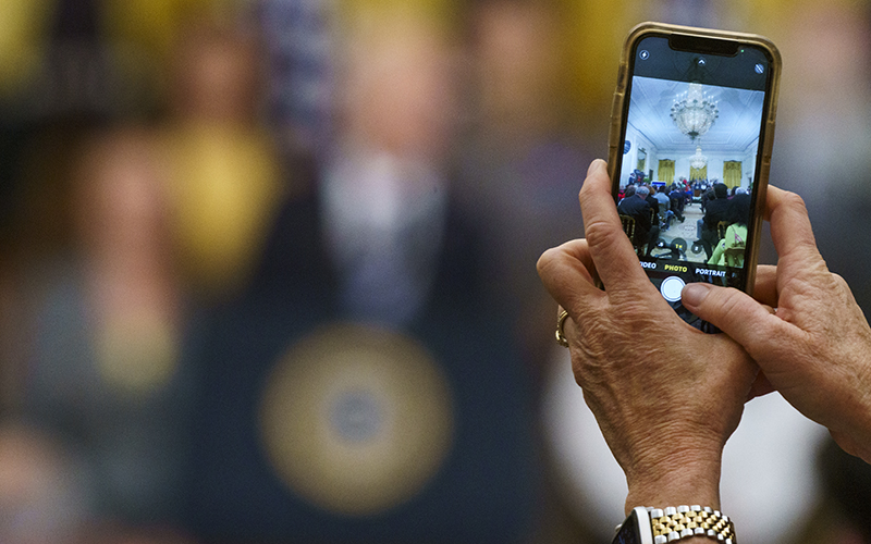 A guest takes a photo of President Biden as gives remarks during a ceremony to mark the anniversary of the Inflation Reduction Act