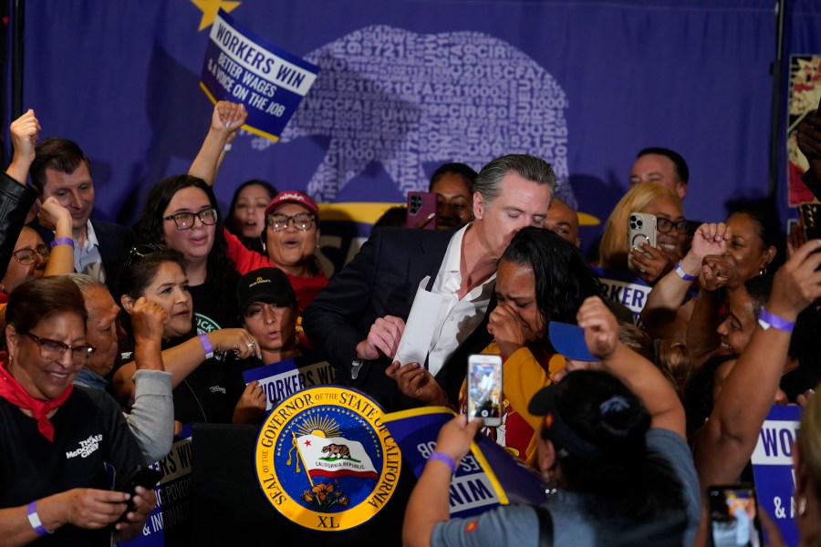 California Gov. Gavin Newsom signs the fast food bill surrounded by fast food workers at the SEIU Local 721 in Los Angeles, on Thursday, Sept. 28, 2023. California fast food workers will be paid at least $20 per hour next year under a new law signed Thursday by Newsom. Anneisha Williams, right, who works at a Jack in the Box restaurant in Southern California celebrates as she holds up the billl. (AP Photo/Damian Dovarganes)