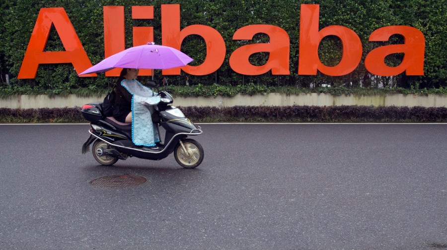 A woman rides a scooter past the company logo outside the Alibaba Group headquarters in Hangzhou, in eastern China's Zhejiang province, May 27, 2016.