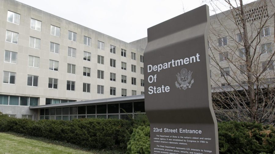 A sign for the Department of State is seen against a building in the background.