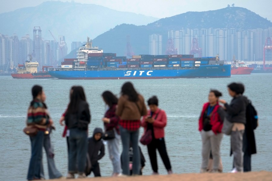 A containers vessel sails by tourists enjoying sea scenery in Xiamen in southeast China's Fujian province on Dec. 26, 2023.