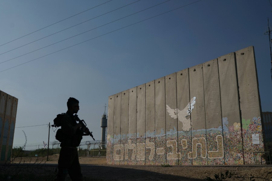 A member of Israeli forces stands next to a security wall with Hebrew writing reading "Path to Peace" at the Kibbutz Netiv Haasara near the border with Gaza Strip, Israel, Friday, Nov. 17, 2023.