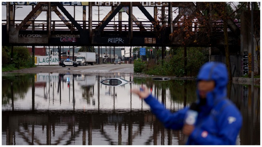 A television reporter does a broadcast as cars are seen submerged on a flooded street under a railroad bridge Thursday, Feb. 1, 2024 in Long Beach, Calif. (AP Photo/Eric Thayer)
