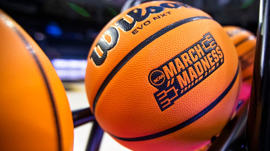 A closeup of a basketball with a March Madness logo is seen on a rack at a game.