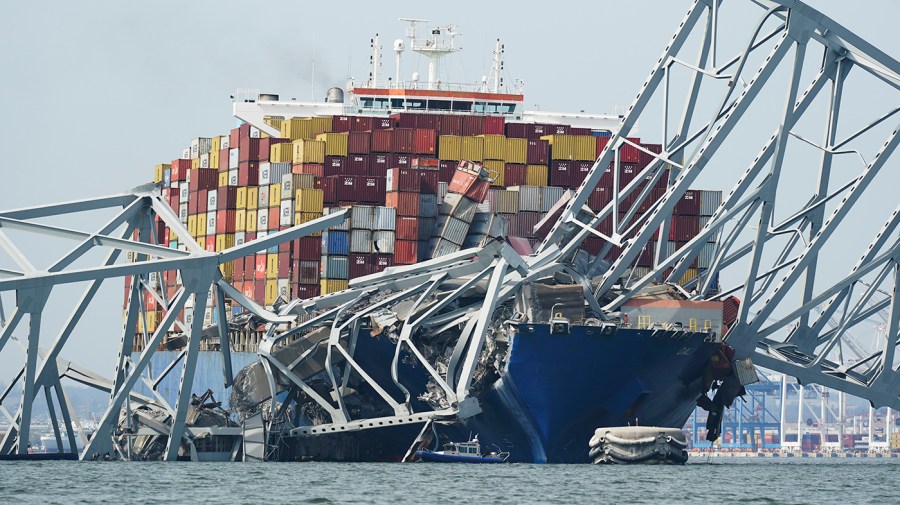 A Coast Guard cutter passes a cargo ship that is stuck under the part of the structure of the Francis Scott Key Bridge after the ship hit the bridge.