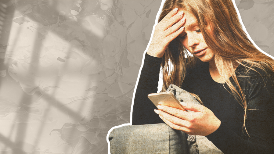 A sitting teen looks down at a phone while holding her head in her hand.